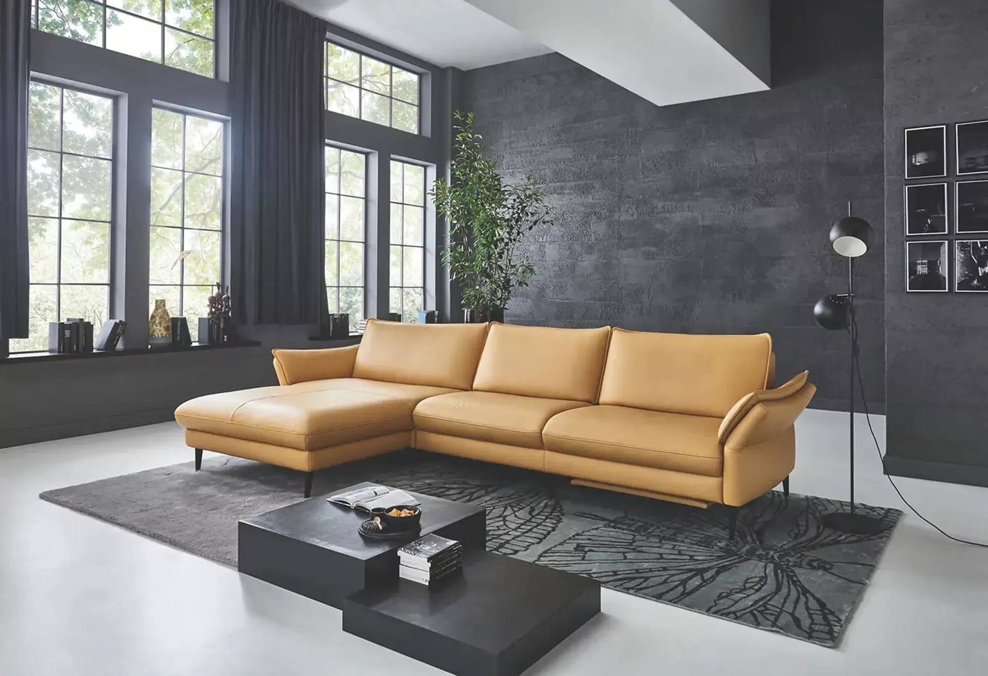 Elegantes cognacfarbenes Ledersofa mit Récamiere in einem modernen Wohnzimmer mit dunkelgrauer Sichtbetonwand